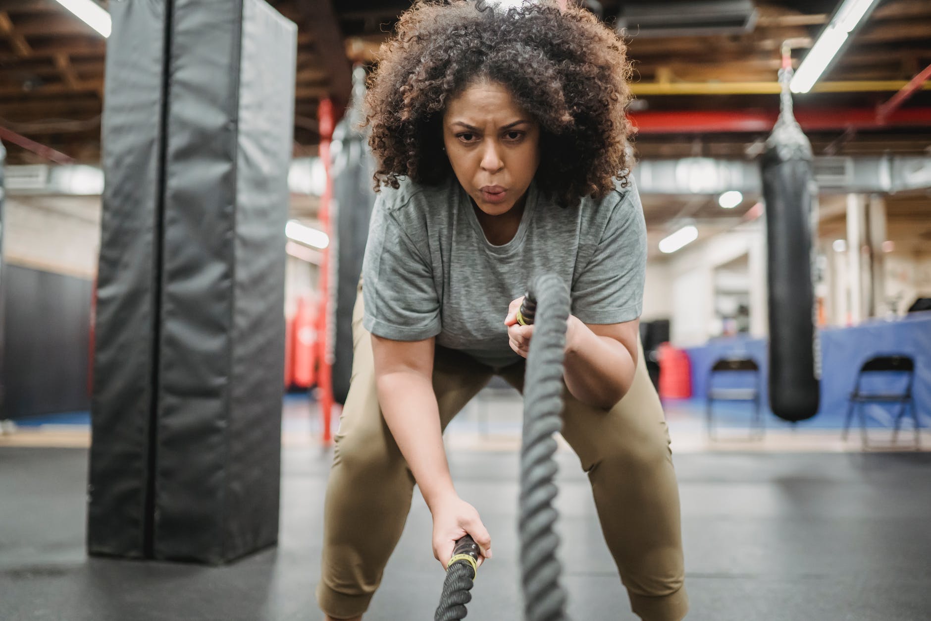 determined black woman exercising with battle ropes in gym