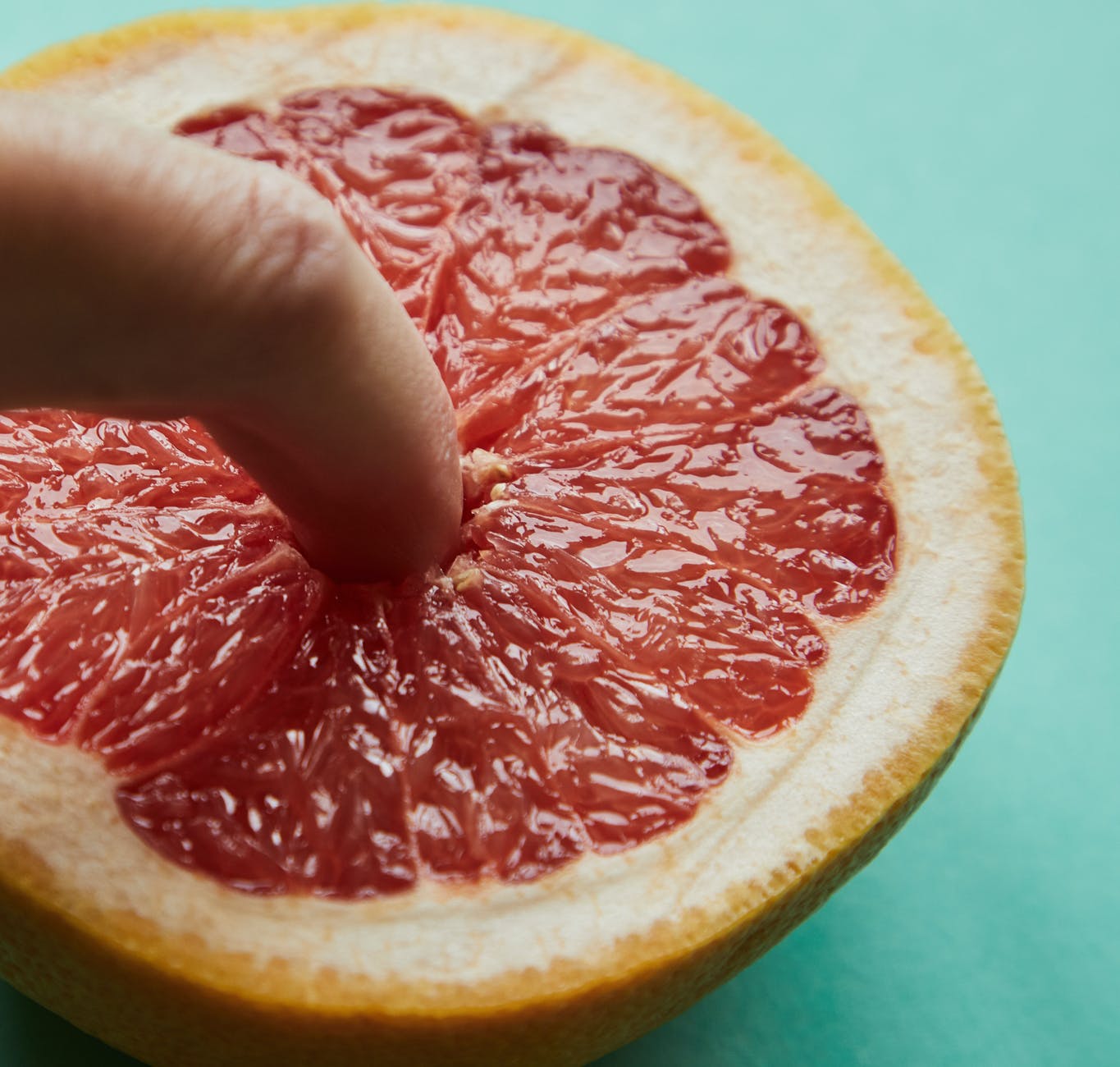 person touching half of ripe grapefruit